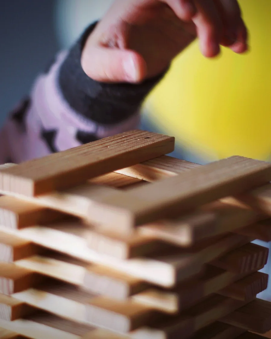 A child's hand reaching over a loose stack of plain wooden planks.